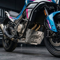A detailed close-up photograph of the brushed silver CNC steel CustomradPH belly pan cover, featuring a distinctive raised "450 MT" logo, installed on the lower section of a CFMOTO 450MT motorcycle. The cover is mounted cleanly below the engine's exhaust headers and behind the front wheel, set against a blurred workshop background to highlight the product's precise fitment.