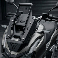 Black powder-coated CNC steel Honda ADV 160 Face Enhancer by CustomradPH installed on the front fairing of a Honda ADV 160. The plug-and-play accessory features a distinct triangular cutout, riveted metal badge, and slotted brackets, seamlessly complementing the scooter's existing angular lines to create an aggressive, structured profile.